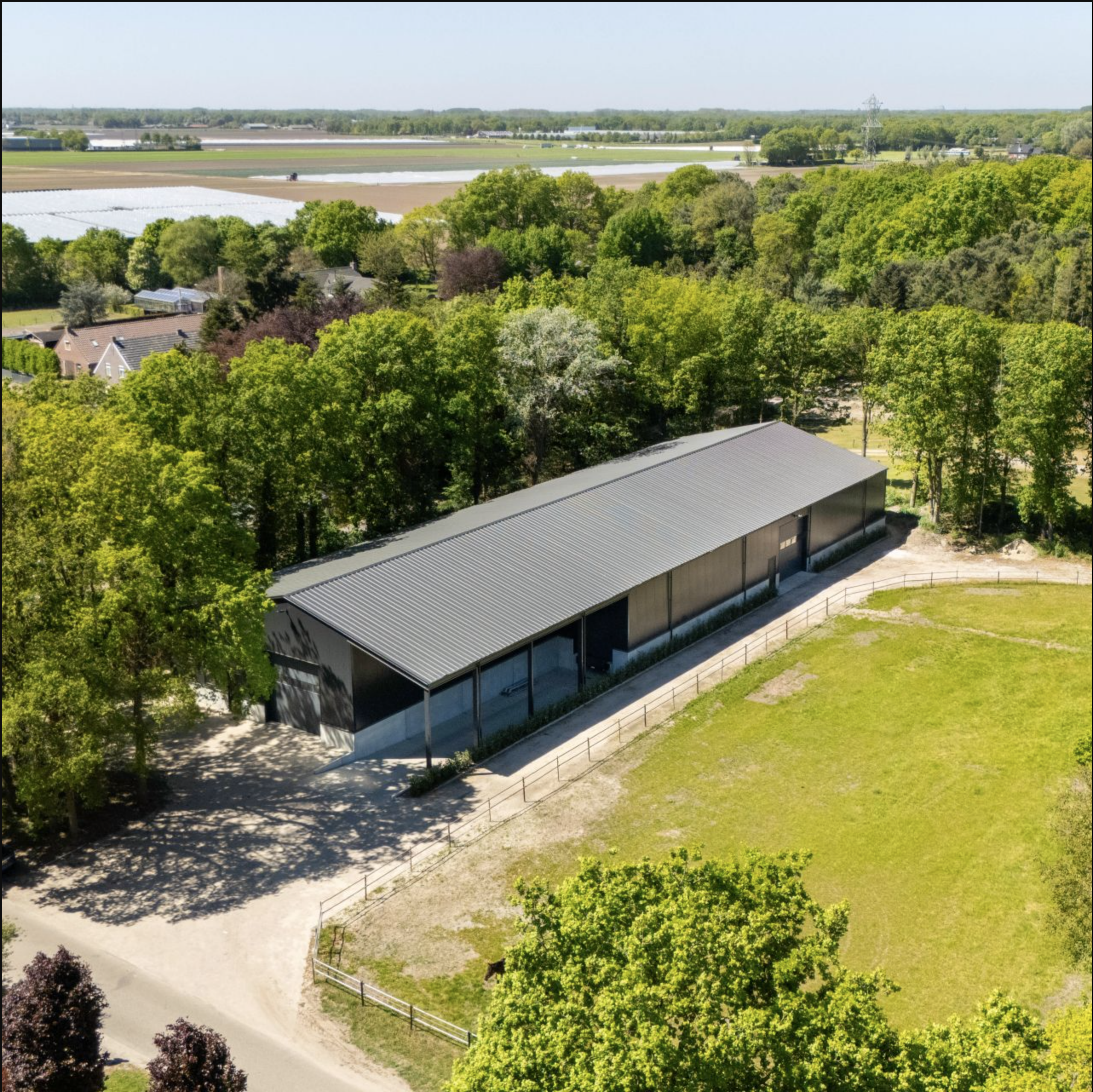 Luchtfoto van de afgewerkte antracietkleurige loods met staande-naad dak en zijluifel, naast een paddock in een groene omgeving